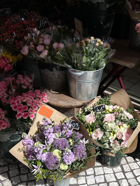 A display of fresh floral arrangements and bouquets arranged on a rustic wooden surface at a flower shop. The selection includes a bouquet of light pink roses with green foliage wrapped in brown paper