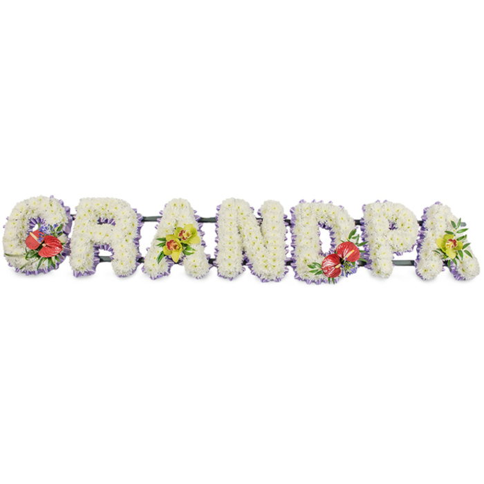 Set against a simple white background, this long funeral flower tribute gently proclaims the word "GRANDPA" in a row of bold capital letters that stretch horizontally like a floral banner of remembrance. Each individual letter is formed from tightly packed white chrysanthemums, their tidy layers of petals overlapping to create a thick, cushion-like surface that feels soft and cloud-light to the eye, symbolising purity, serenity, and a peaceful farewell. A fine edging of pale lavender ribbon runs along the base of every letter, appearing as a subtle lilac band that both frames and grounds the design, adding a note of tranquillity without distracting from the clean white blooms. A dark green support frame discreetly anchors the letters from behind, keeping the tribute secure for display at a St John's Wood funeral, burial, or memorial service. To introduce personality and depth, the florist has woven in distinctive accent sprays at key points. The "G" and "D" carry dramatic clusters of deep red anthuriums, their smooth, heart-shaped spathes shining with a gentle gloss and punctuated by bright, upright spadices, all nestled among rich green foliage and a scattering of small purple filler flowers that echo the lavender trim and tie the colours together. The first "A" and the final "A" are softened by elegant yellow-green orchids, their graceful blooms and muted lime tones resting on polished leaves, suggesting gratitude, affection, and cherished memories. This floral word tribute could easily be envisioned at a service for a much-loved grandfather, perhaps one who enjoyed quiet mornings in Regent's Park or outings along Hamilton Terrace. It is a thoughtful, handcrafted arrangement that speaks gently of love, respect, and the lasting imprint of family.