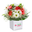 A splash of spring energy, this radiant bouquet from St John's Wood Flowers is gathered into a crisp white gift bag that promises both surprise and delight. Coral and vivid red carnations play the lead role, each bloom ruffled and lush, unfurling layers like laughter on a sunny day at Lord's cricket ground. White daisies, punctuated with bright green centers, bring a light-hearted contrast, their petals sparkling as if caught in morning light drifting through St John's Wood's leafy streets. Wispy sprays of baby's breath swirl throughout the bouquet, their petite blossoms lending innocence and a cloud-like softness to the arrangement. On one side, tiny purple-tinged buds rest quietly, suggesting stories still to unfold. Surrounding all, a flourish of deep green, shiny foliage wraps the base, gathering the flowers with a sense of both order and abundant joy. The bouquet's round, overflowing shape tells of expert hands and a love for making ordinary days exceptional. Set within the structured white bag with strong ribbon handles and shown against a pure white backdrop, it's an invitation to celebration, cheer, and genuine local warmth-ideal for birthdays, heartfelt thank-yous, or welcoming a new neighbour on Grove End Road.