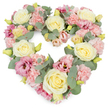 A soft, romantic heart-shaped wreath is shown against a pure white background, its pastel colours and rounded lines creating an immediate sense of calm and affection. Every part of the heart is densely filled with flowers, so the surface appears plush and comforting, like a floral embrace. Creamy ivory and pale yellow roses are the most prominent blooms, their layered, spiralling petals forming generous cups that bring structure and serenity to the design. Nestled between them are clusters of light pink carnations, their many frilled petals overlapping in little waves, adding both volume and an airy, billowing texture. Deeper pink and mauve lisianthus flowers are scattered throughout, their more open, trumpet-like forms and richer tones adding a gentle contrast that keeps the eye moving softly around the heart. Silver-toned eucalyptus leaves curve through the arrangement, their smooth, rounded foliage in muted blue-green tracing the outline and threading between blossoms with quiet grace. Tiny yellowish-green buds peek from the floral mass, subtle reminders of growth and new beginnings. The overall mood is one of quiet remembrance, perfect for a funeral, memorial, or celebration of life in St John's Wood, perhaps near the tree-lined paths leading to Regent's Park or the calm spaces around local chapels. Crafted with care, this heart-shaped tribute expresses sympathy, gratitude, and enduring love, offering a peaceful focal point for family and friends as they gather to honour someone who meant a great deal to them.